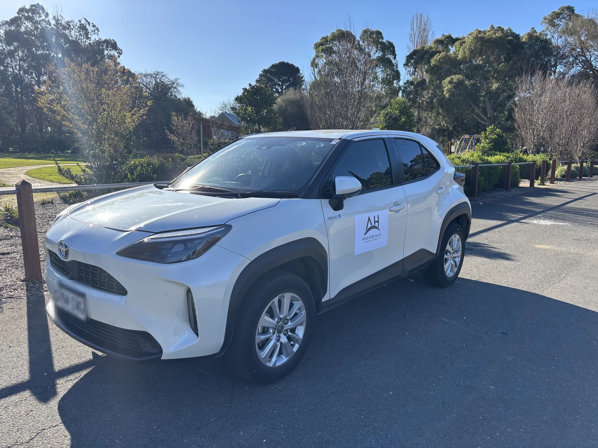 The Adelaide Hills Driving School Toyota Yaris Cross hybrid dual-control car, signed with the AH logo and parked among gum trees